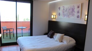 A hotel room with a large bed, a small table, and a chair near a sliding glass door leading to an outdoor area. - Hôtel l'Hacienda (Chateauneuf-les-Martigues)