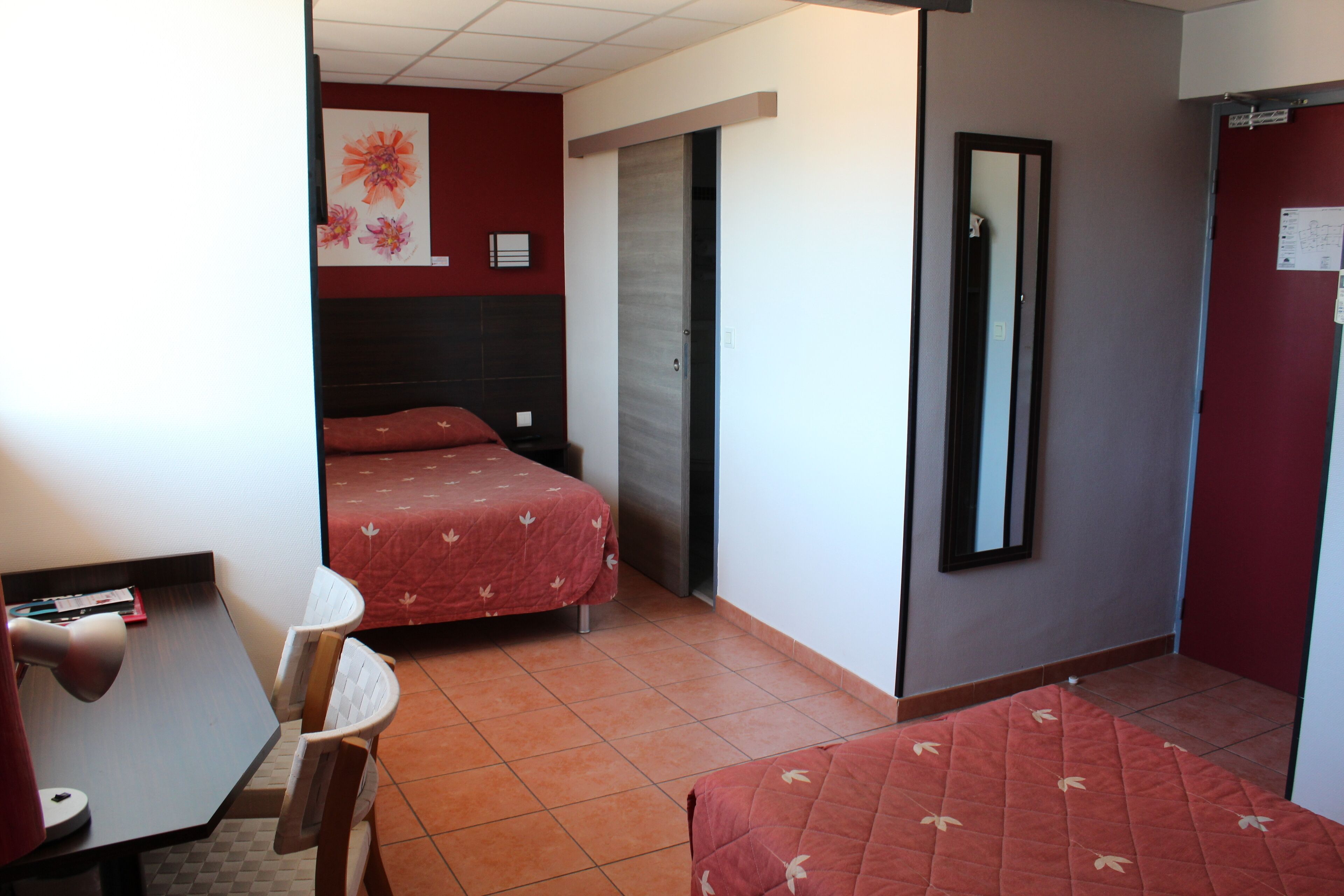 A hotel room with two beds, a desk, a chair, and a mirror.