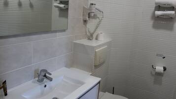 Un bagno con lavandino, specchio e water bianchi. Asciugamani e un asciugacapelli sono montati a parete.