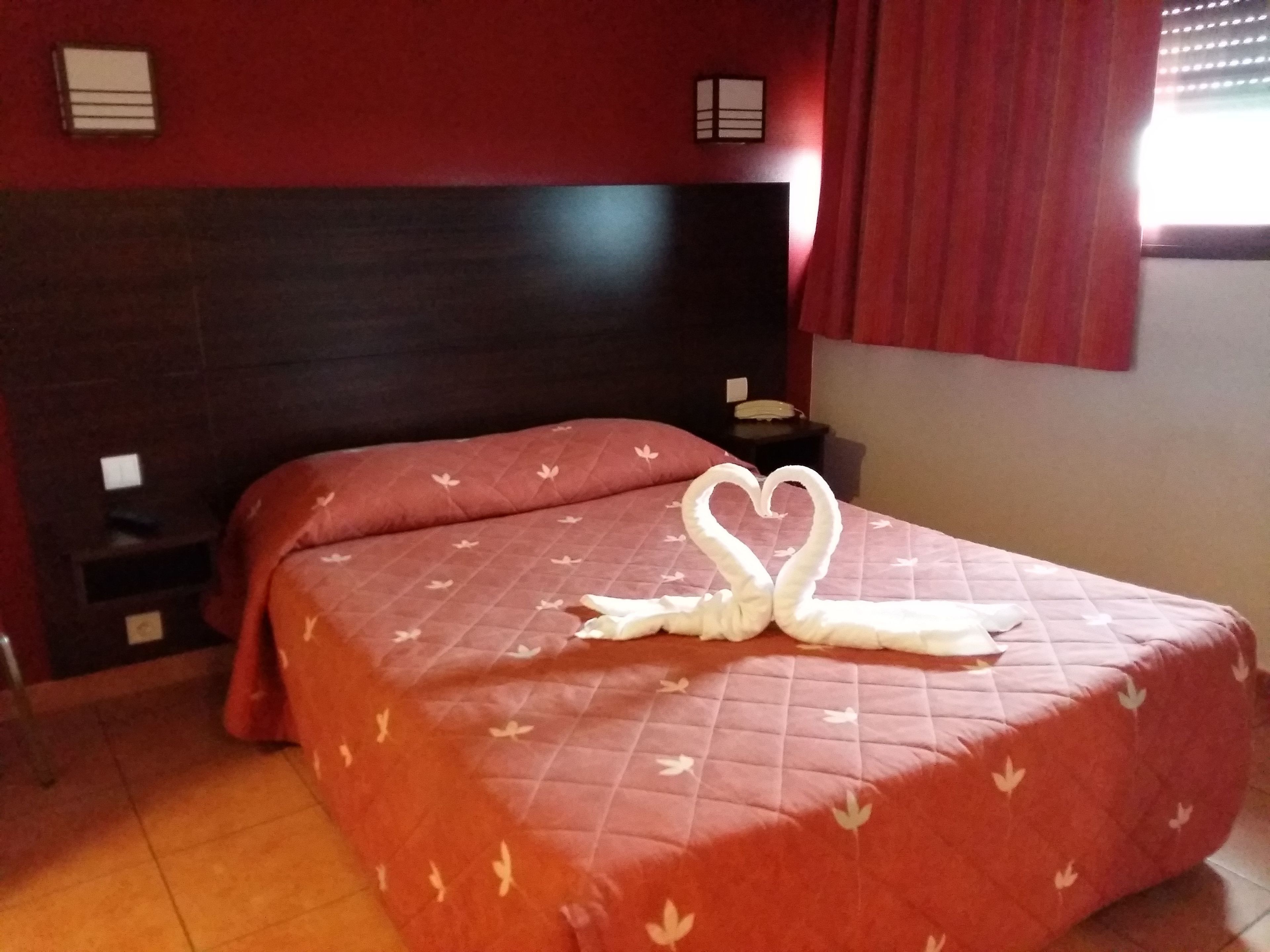 A hotel room with a bed, a headboard, a nightstand, and a red curtain.