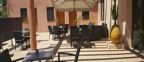 Une terrasse extérieure avec des tables et des chaises, un grand parasol et des plantes en pot.