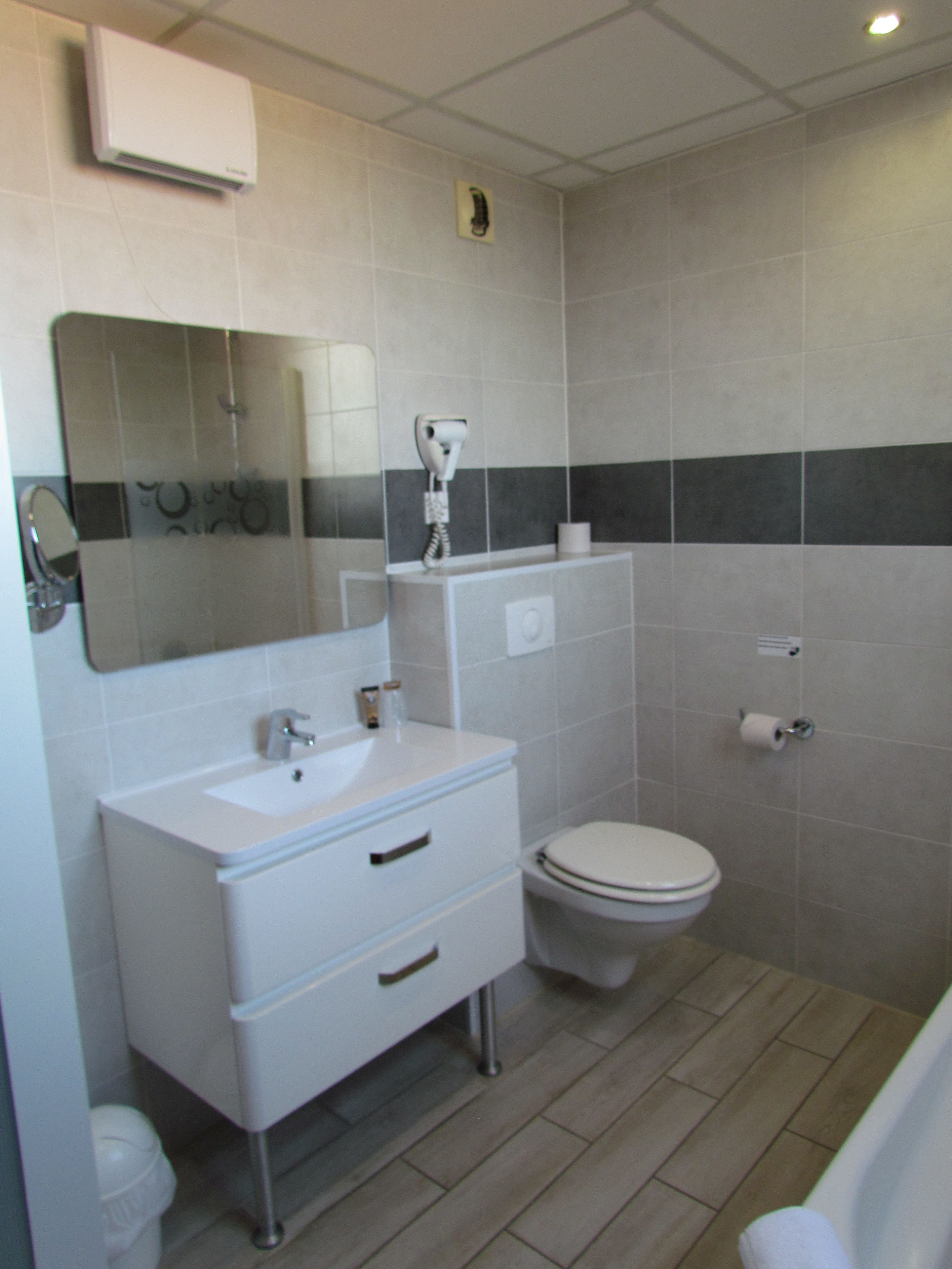 Baño con lavamanos, espejo, inodoro y secador de pelo en la pared.