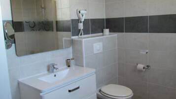 Baño con lavamanos, espejo, inodoro y secador de pelo en la pared.