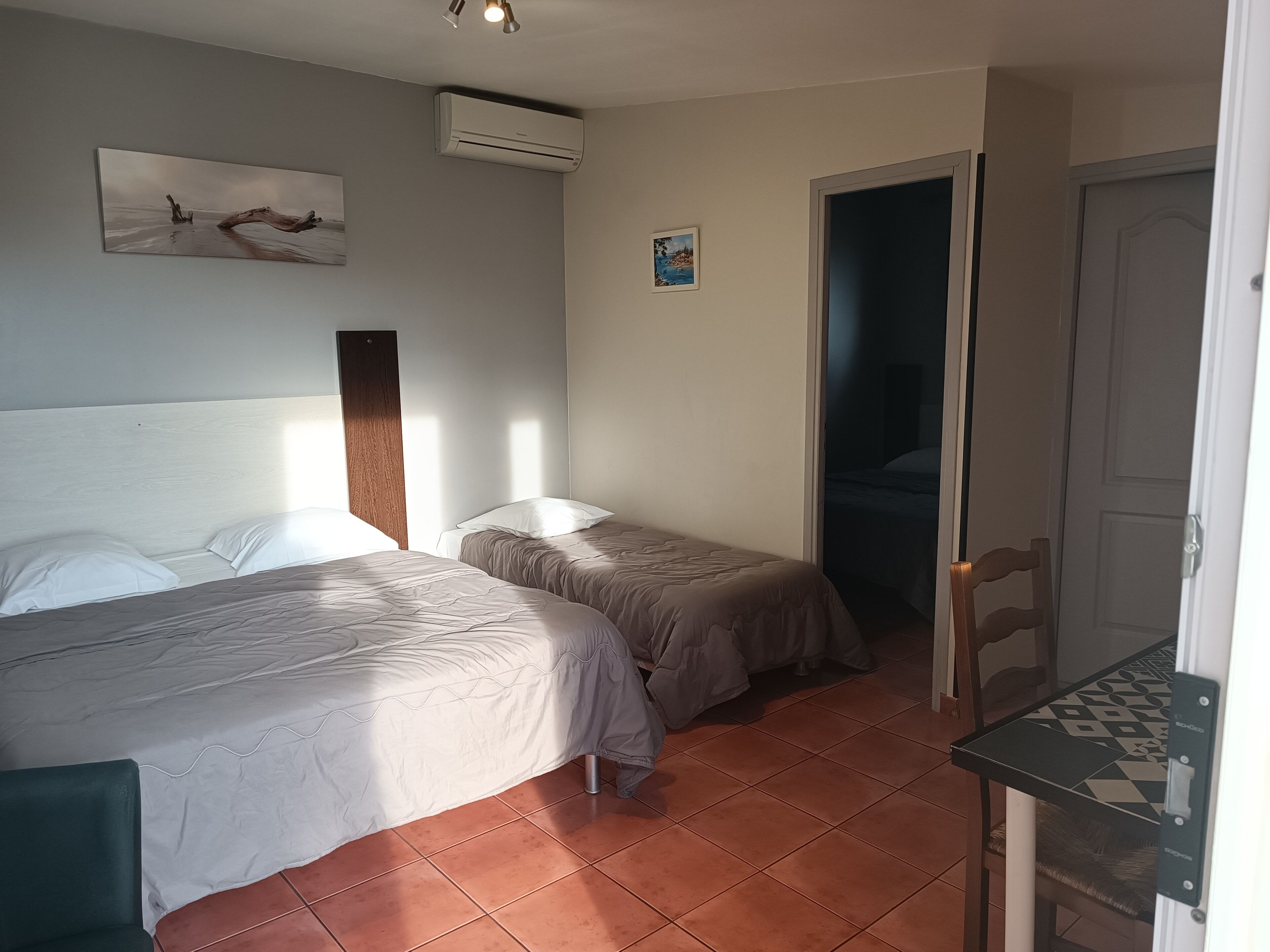 A room with two beds, a wooden headboard, an air conditioner, and a door leading to another room.