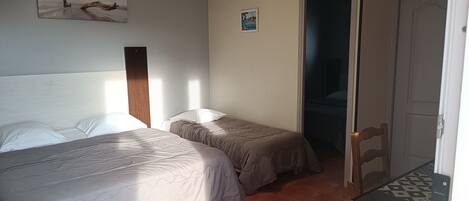 A room with two beds, a wooden headboard, an air conditioner, and a door leading to another room.