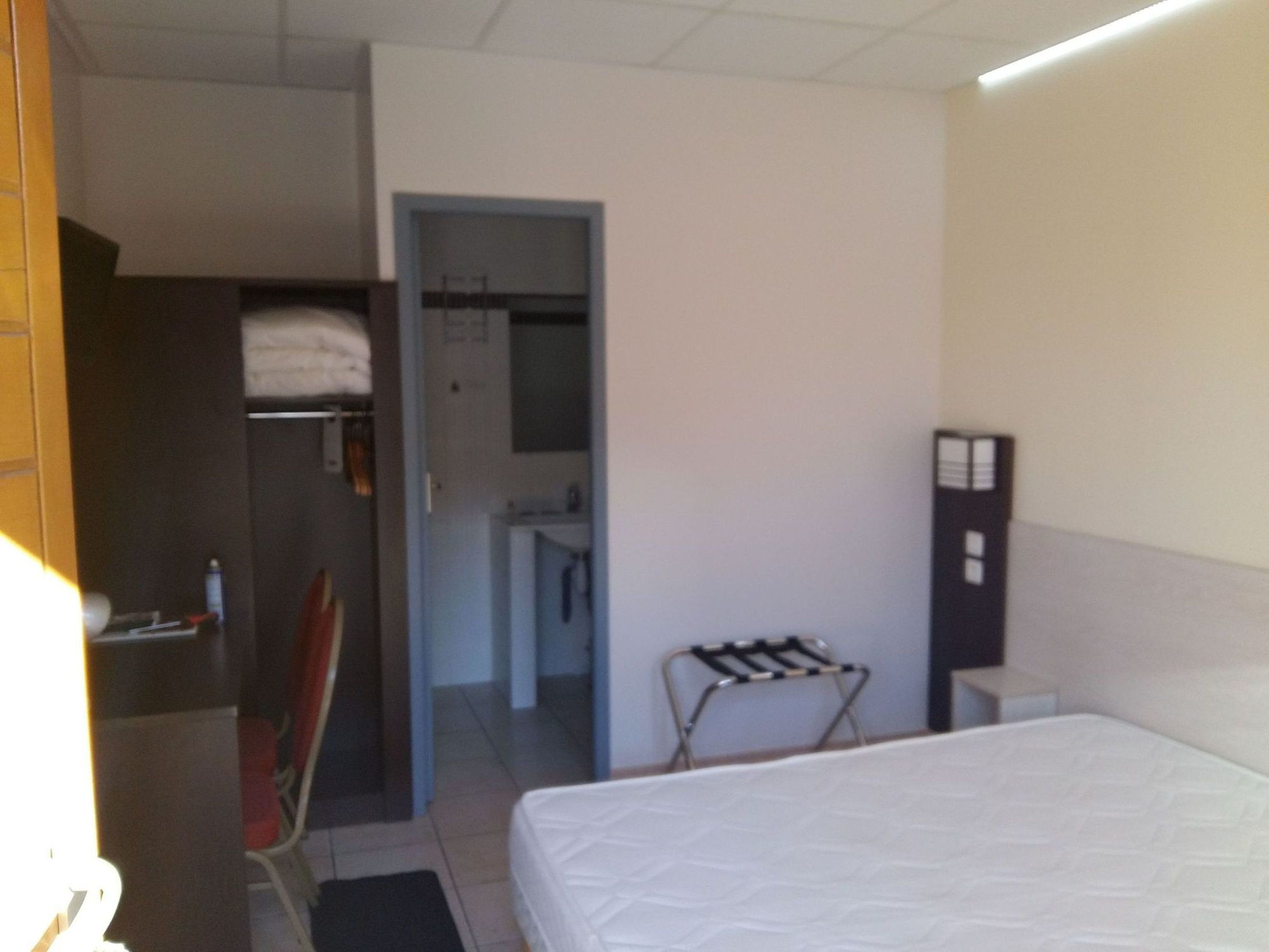 A hotel room with a bed, a chair, a small table, a wardrobe, and a bathroom visible through an open door.