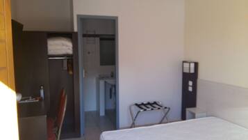 A hotel room with a bed, a chair, a small table, a wardrobe, and a bathroom visible through an open door.