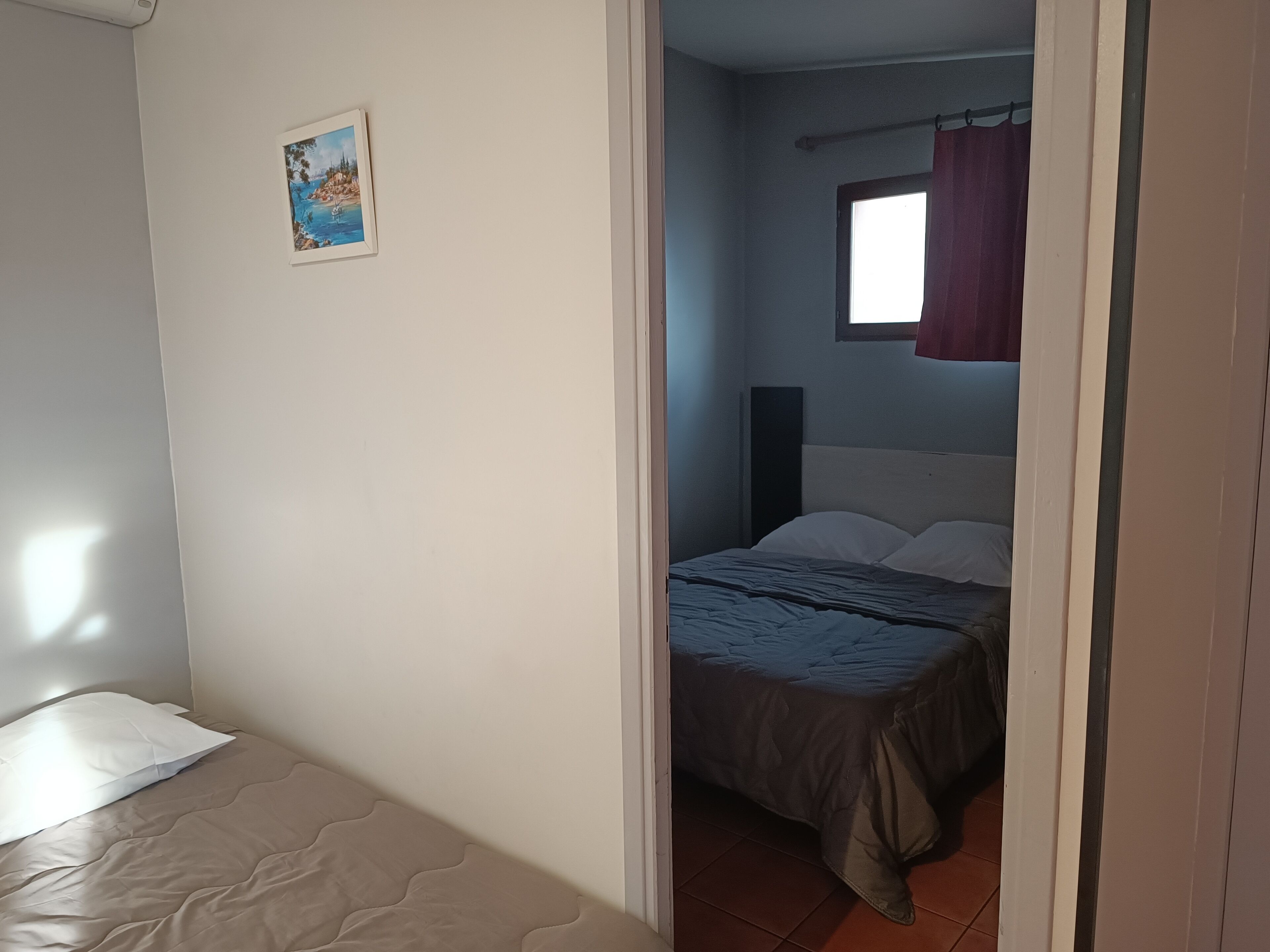 A bedroom with a bed, a small window with a curtain, and a wall-mounted picture.