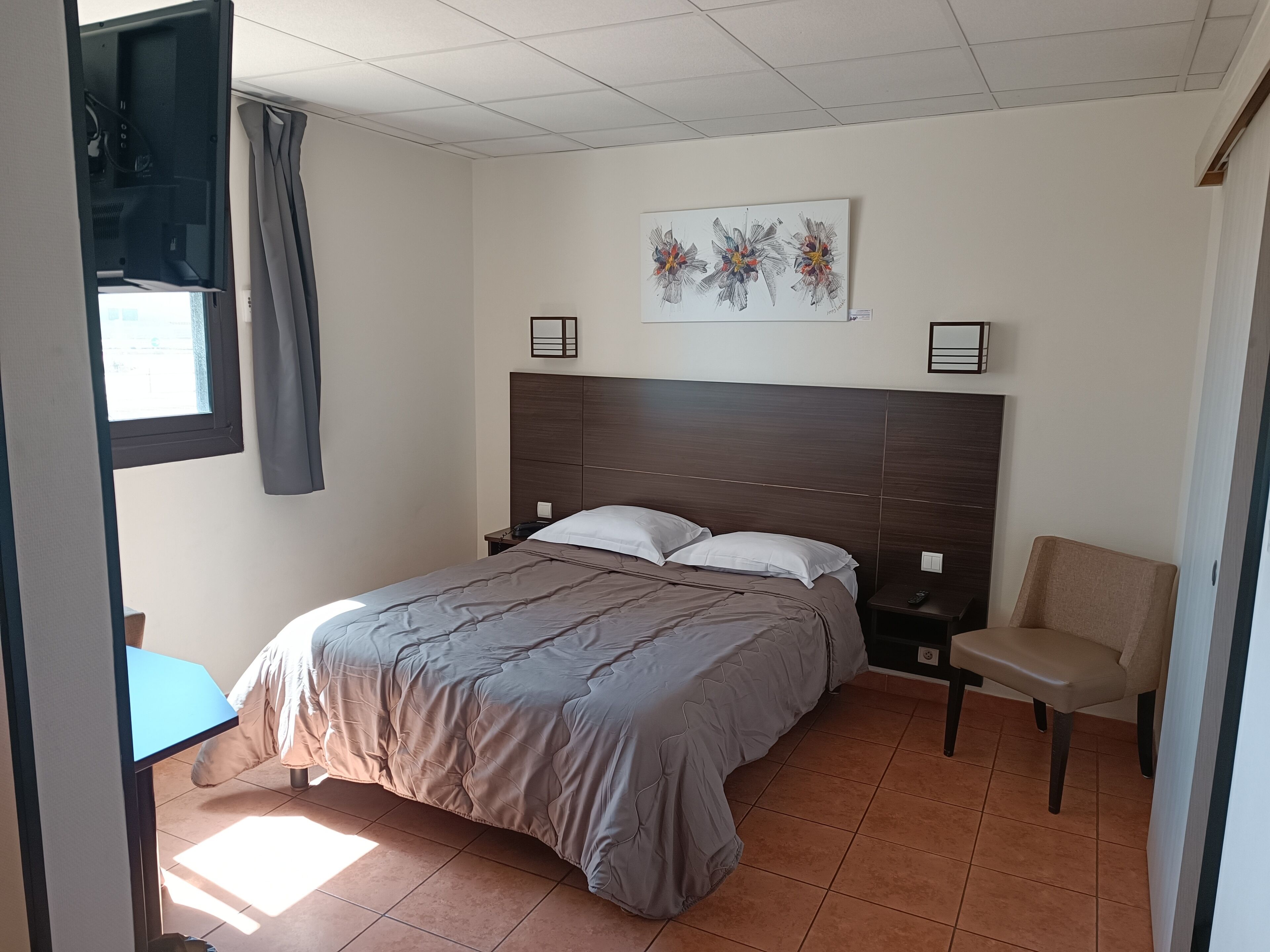 A bedroom with a bed, a chair, a nightstand, a painting, and a window with curtains.