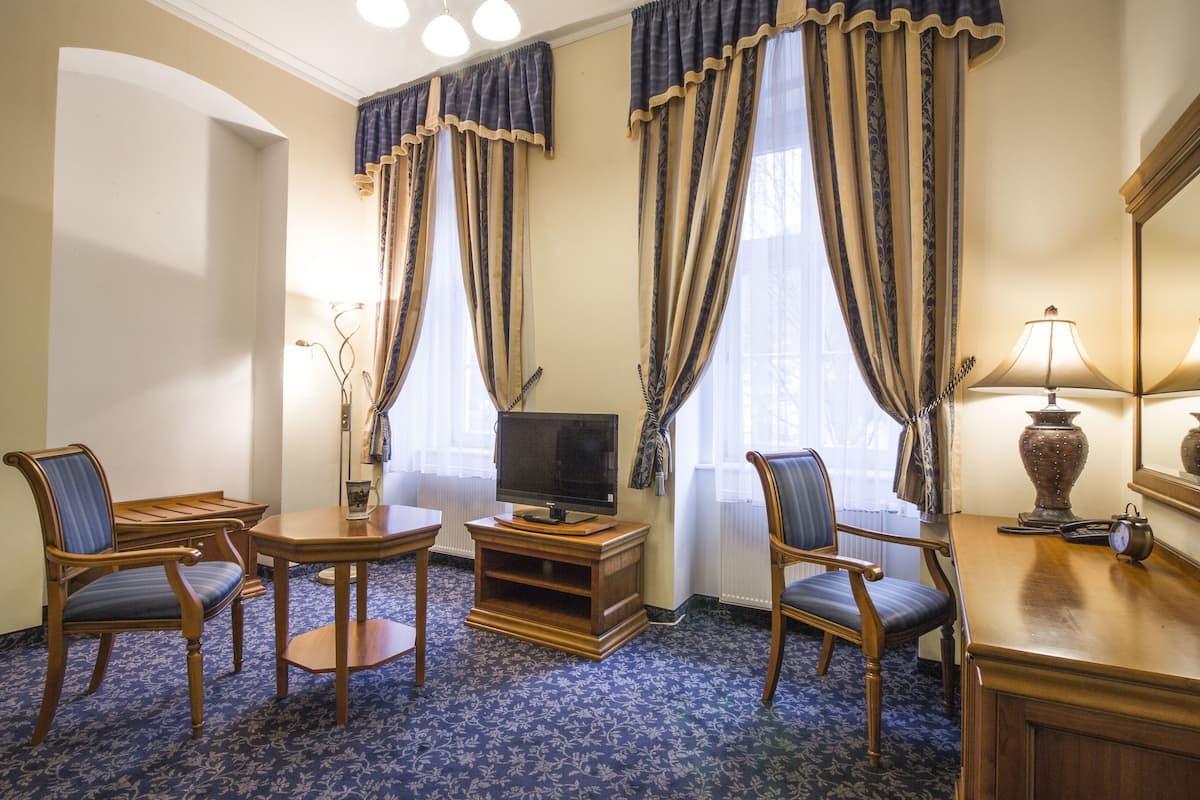 Une chambre d’hôtel équipée d’une télévision, de deux fauteuils, d’une petite table, d’une lampe et d’une grande fenêtre avec des rideaux.