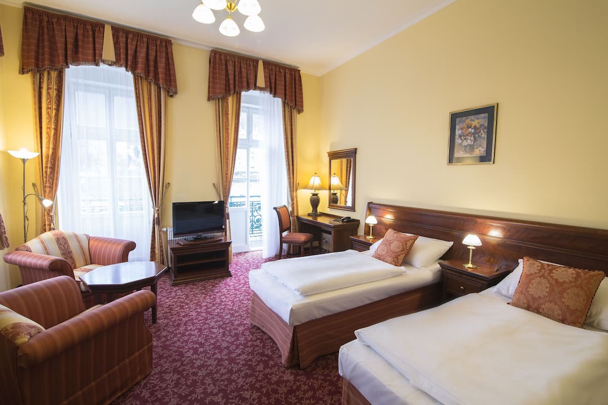 Une chambre d’hôtel avec deux lits, un bureau, une télévision et un coin salon comprenant un canapé et des fauteuils.
