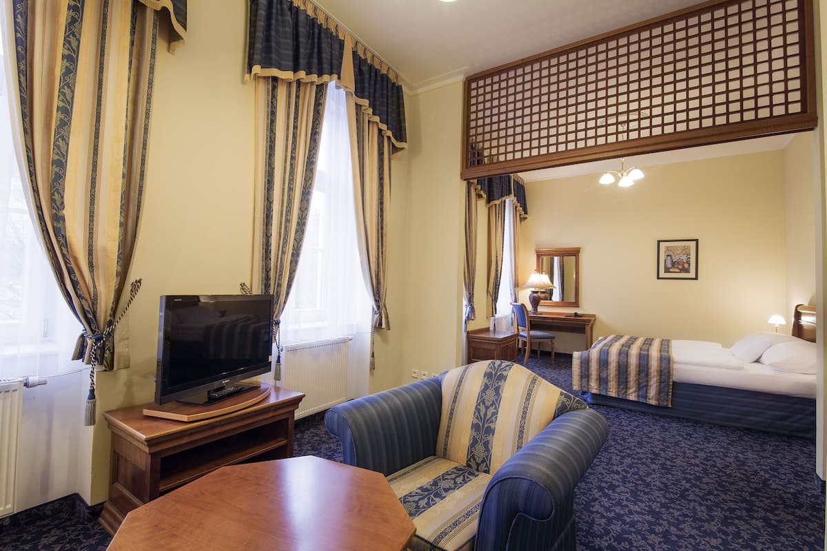 Une chambre d’hôtel équipée d’un téléviseur posé sur un meuble en bois, d’un canapé, d’un lit, d’une table à manger et d’un paravent décoratif.