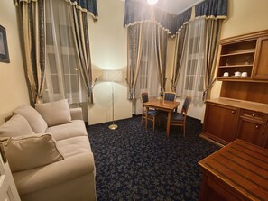 Une chambre d’hôtel comprenant un canapé, une table à manger avec des chaises, une lampe et un meuble avec des étagères.