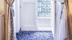 Ein Zimmer mit blauem Teppich mit Muster, einer weißen Tür und Blick auf einen Balkon mit Metallgeländer.