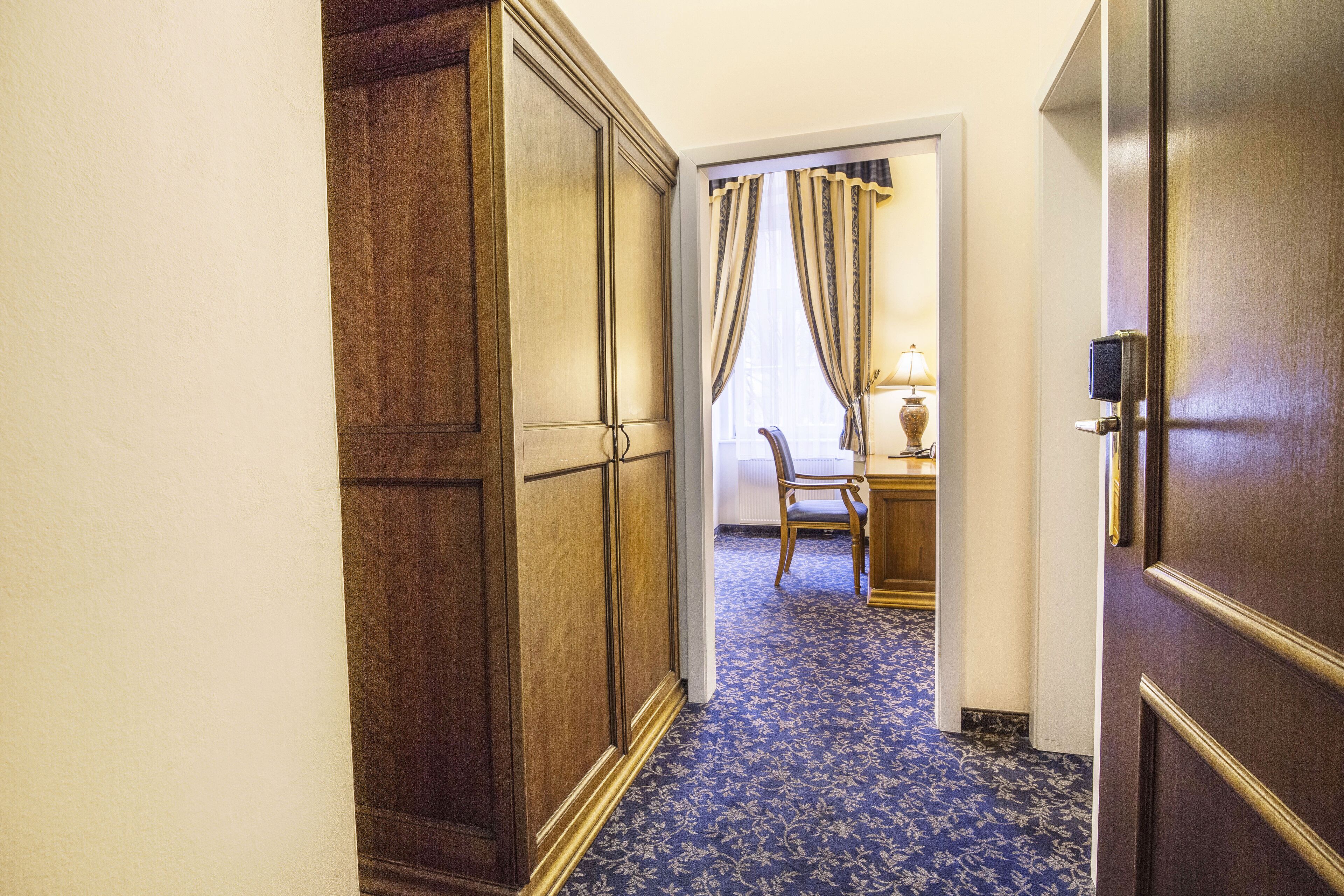 A hallway with a wooden wardrobe, a desk with a lamp, and a chair.
