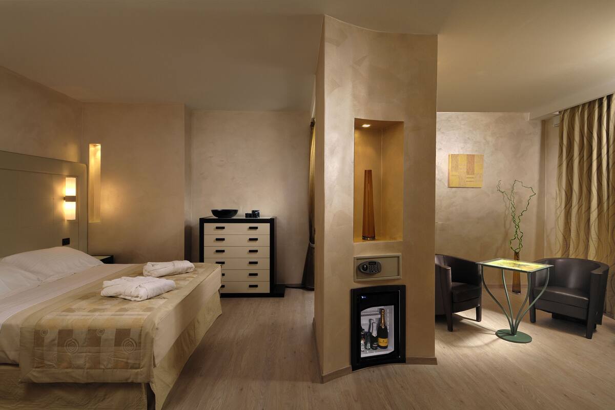 A hotel room with a bed, a dresser, a small table with a vase, and two chairs.