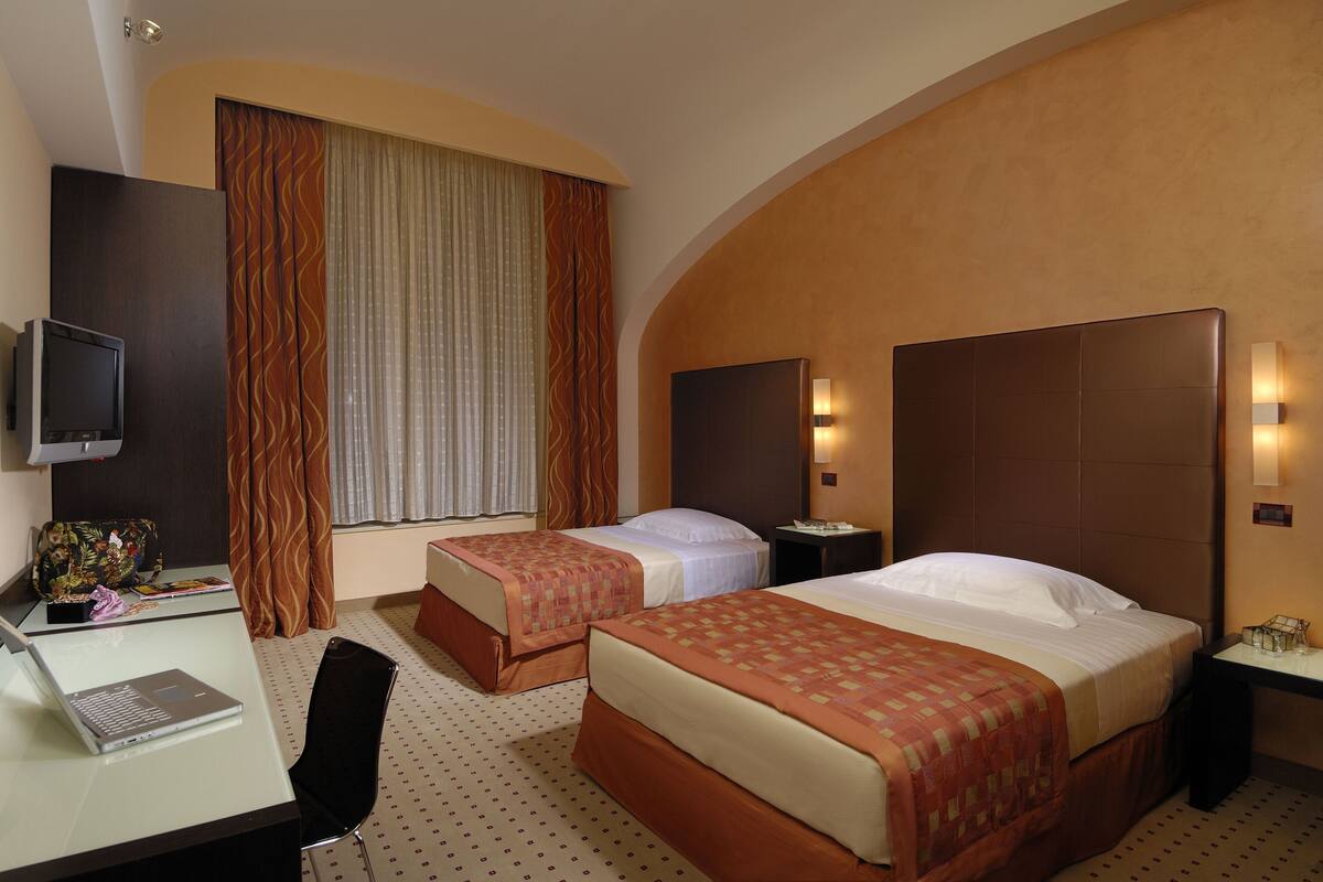 A hotel room with two beds, a desk with a laptop, a TV, and a chair.