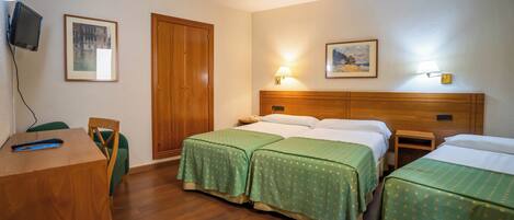 Ein Hotelzimmer mit zwei Betten, einem Schreibtisch, einem Sessel, einem Fernseher und zwei gerahmten Bildern an der Wand.