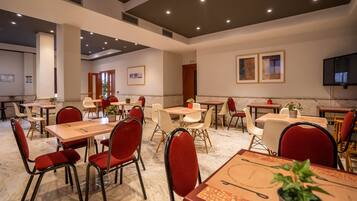 A spacious dining area with multiple tables and chairs, marble flooring, and framed artwork on the walls.