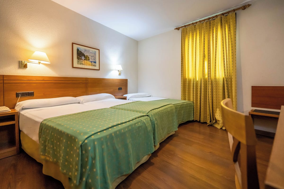 A hotel room with two beds, wooden headboard, bedside lamps, a painting on the wall, and a curtain.