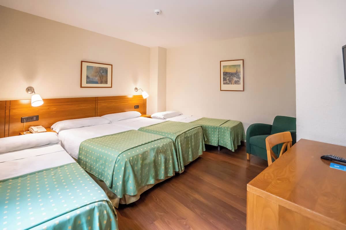 A hotel room with three single beds, a wooden table, and two chairs.