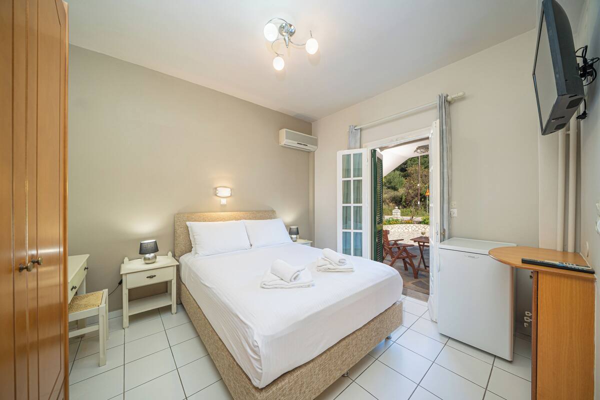 Un dormitorio con cama, mesita de noche, lámpara, aire acondicionado y un refrigerador pequeño.
