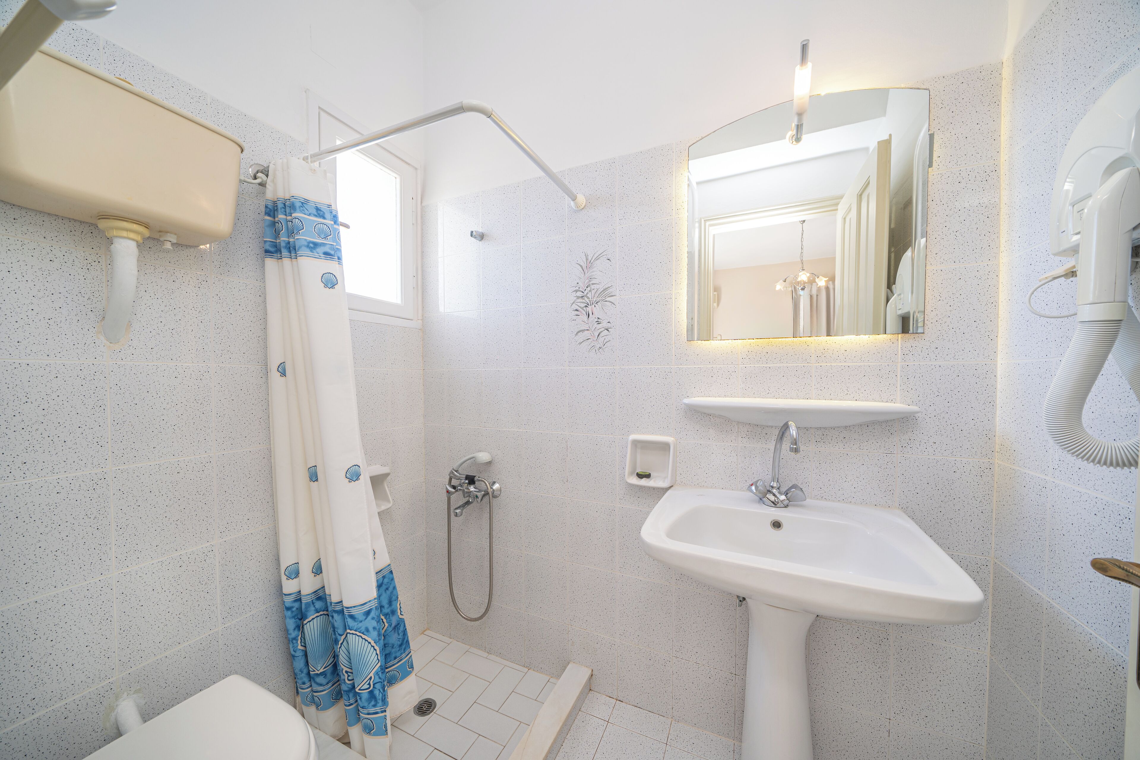 A bathroom with a shower, toilet, sink, and a mirror.