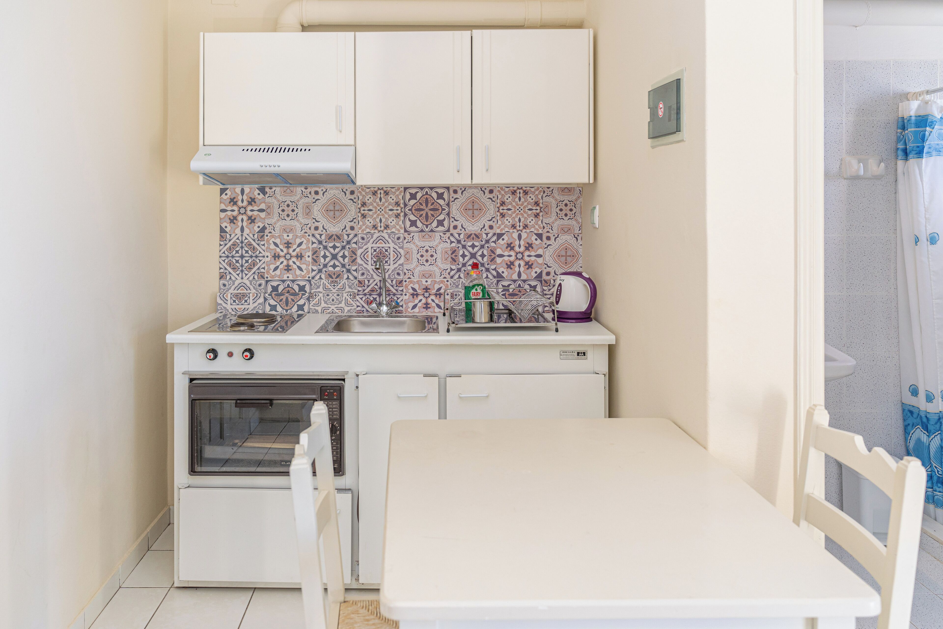 A compact kitchen with a stove, oven, sink, and a small dining table with chairs.