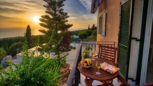 A balcony with a table set for two, overlooking a swimming pool and lush greenery. - Panoramic Sunset (Kefalonia)