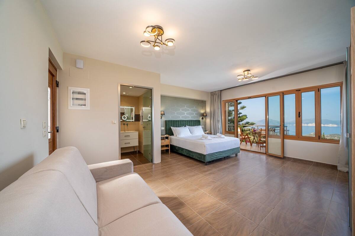 Un dormitorio moderno con una cama grande, una zona de estar, un baño y un balcón con vistas al mar.