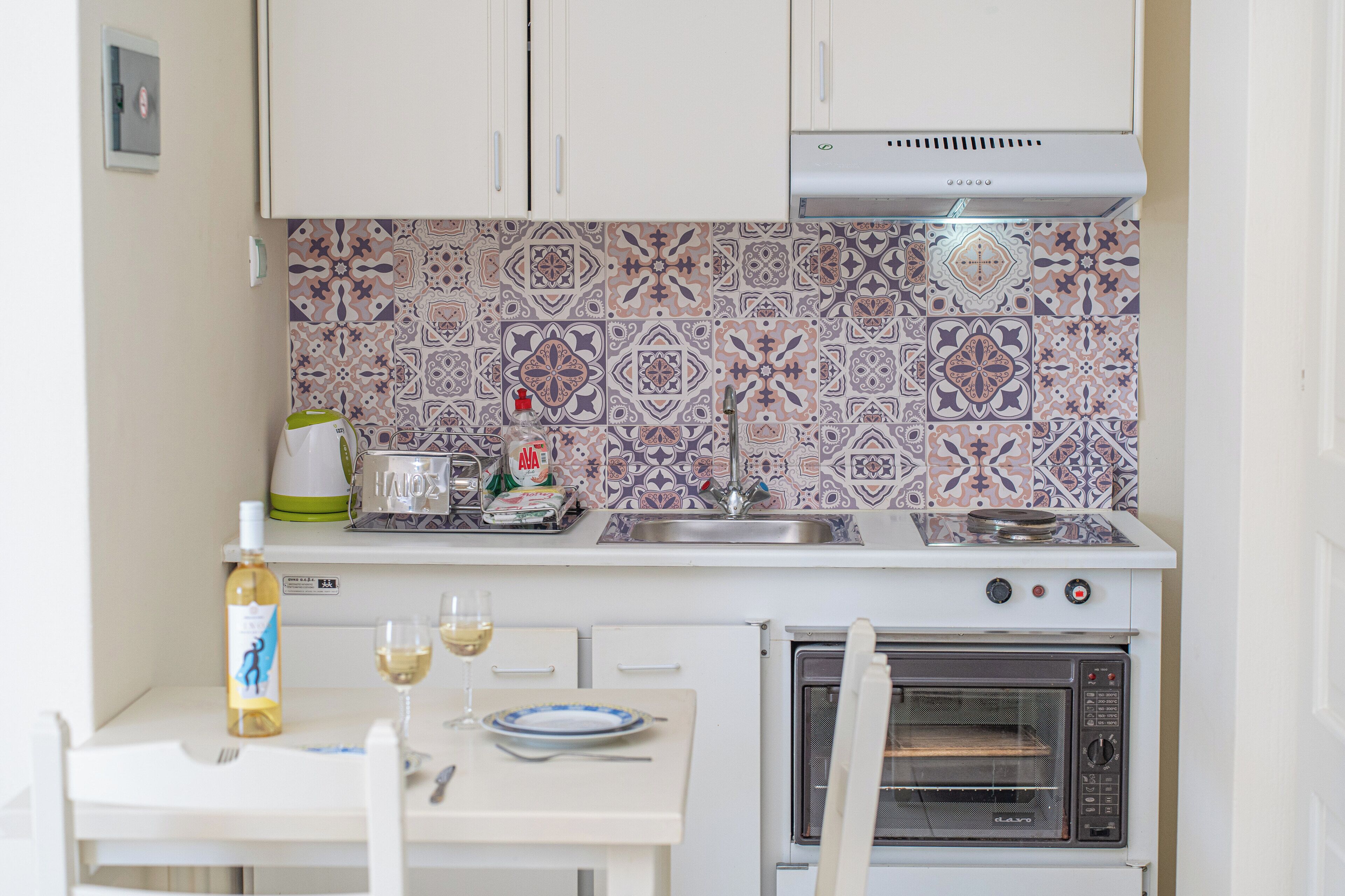 Una cocina compacta con horno integrado, un lavamanos y un salpicadero de azulejos.
