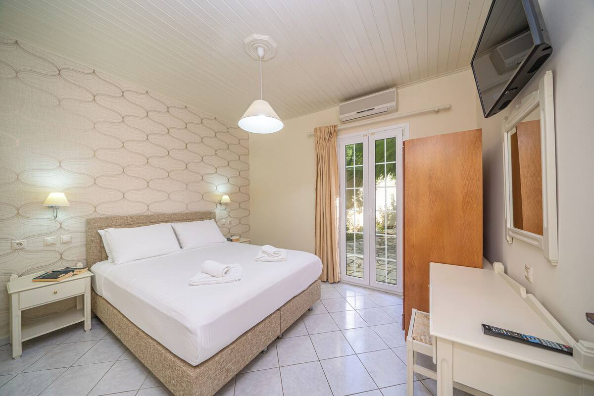 Un dormitorio con cama, mesitas de noche, televisor y puerta corrediza de vidrio que da a un espacio exterior.