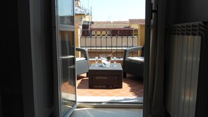 A balcony with wicker furniture, a table with a bottle of champagne, and a tiled floor. - Hotel Indipendenza (Rome)