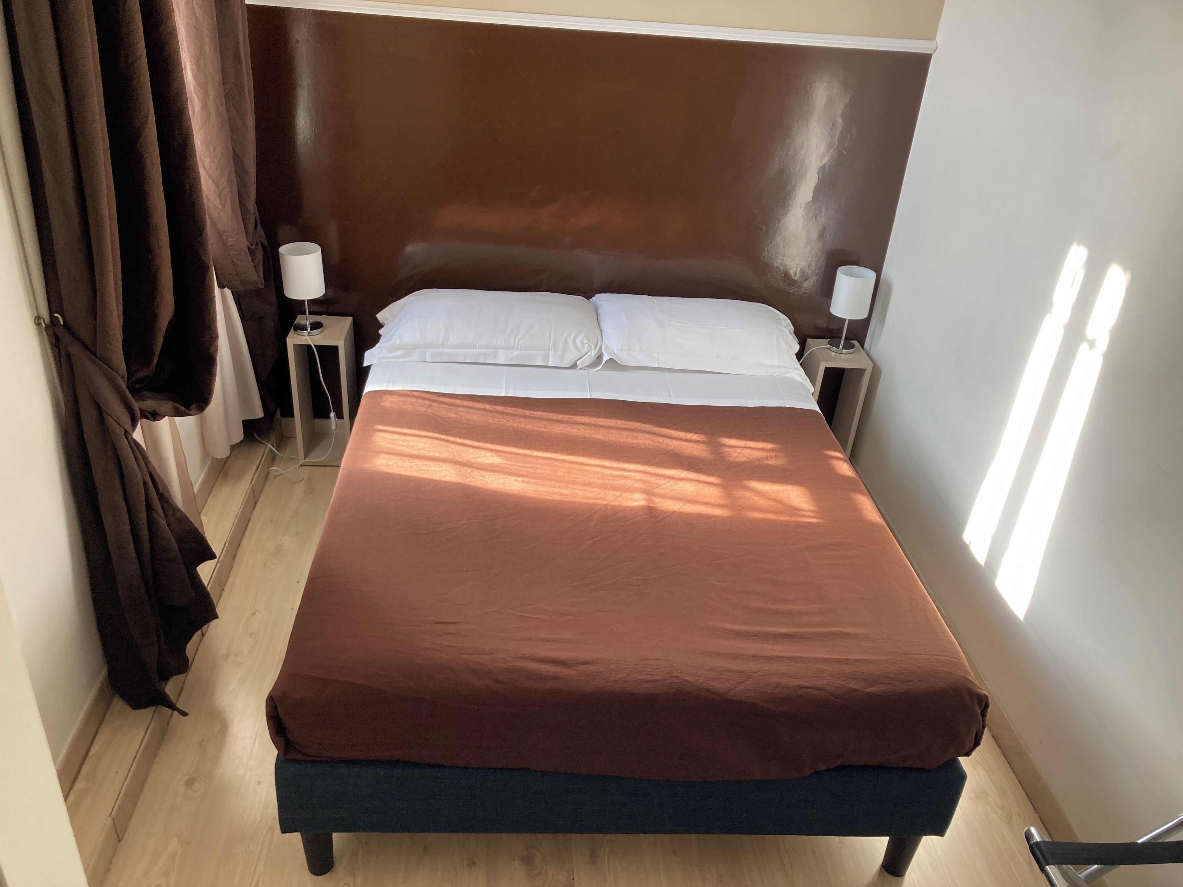 A neatly made bed with a brown cover, two bedside lamps, and a wooden floor.