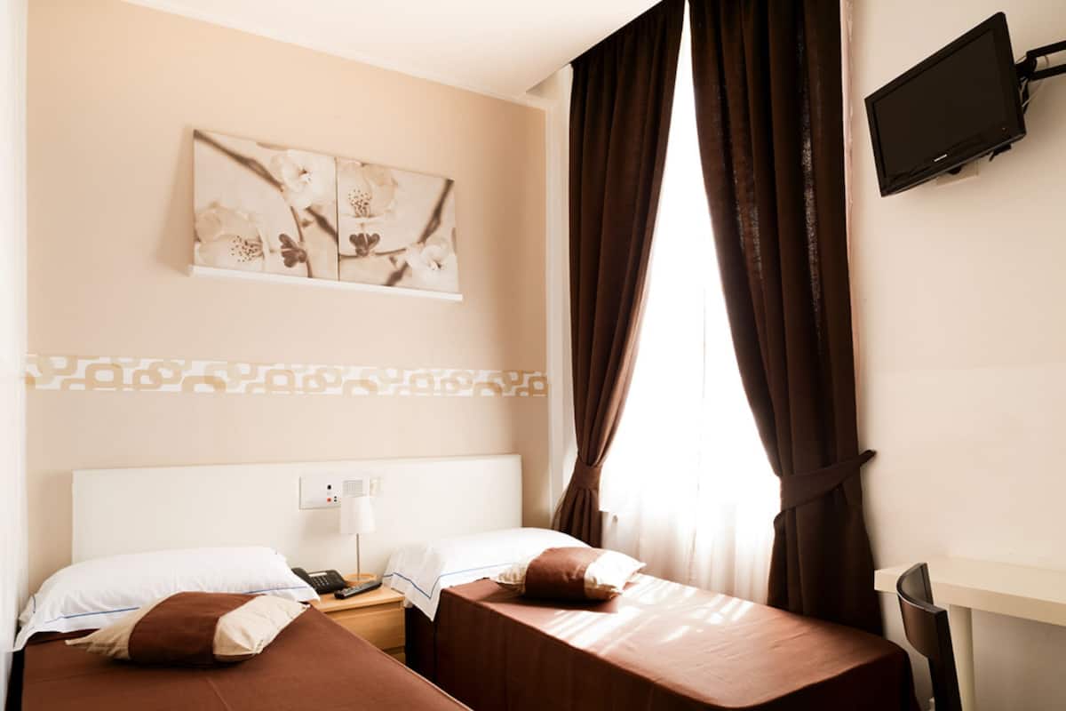 A hotel room with two beds, a flat-screen TV mounted on the wall, and a window with curtains.