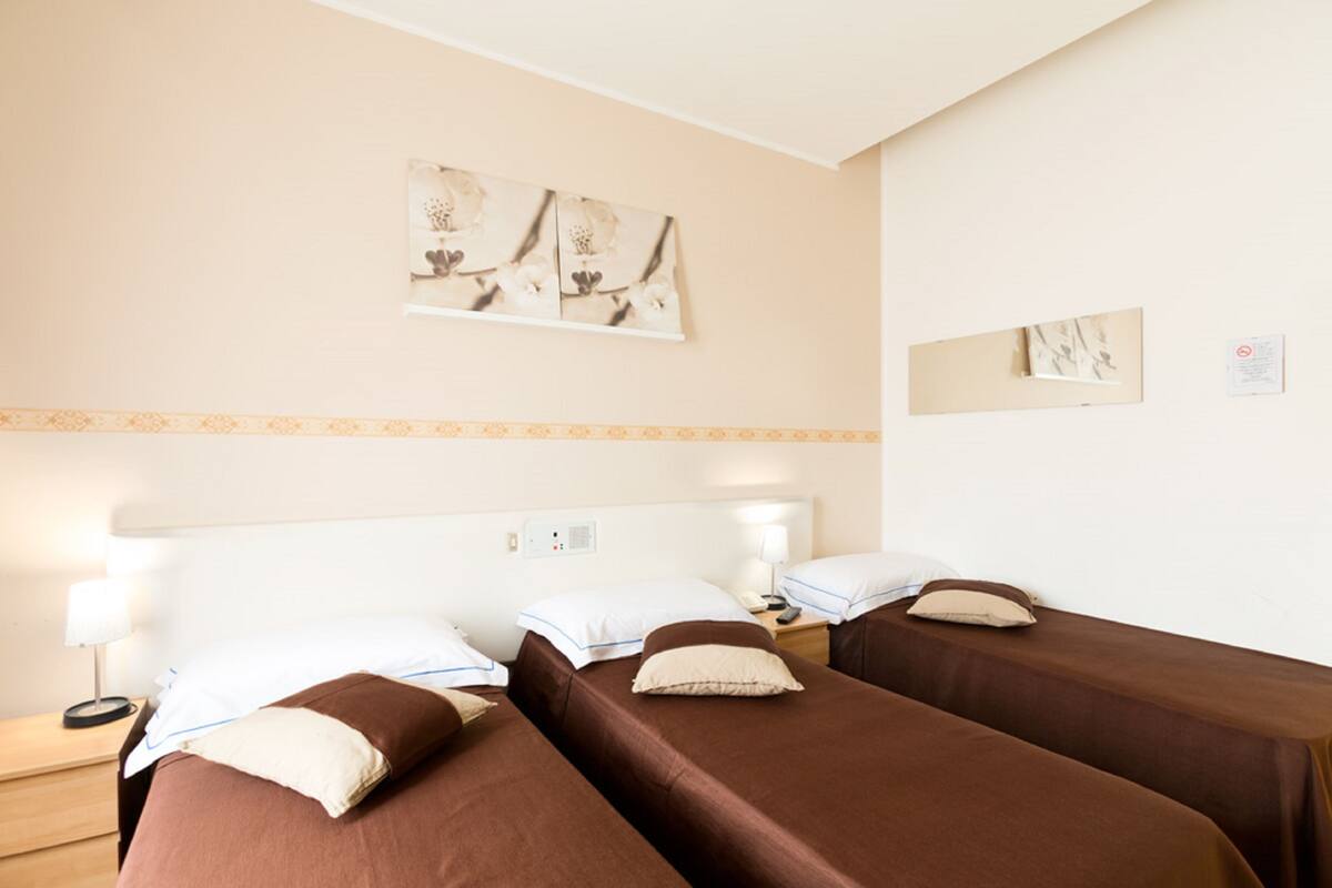 A hotel room with two single beds, a nightstand with a lamp, and a wall-mounted artwork.