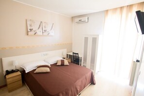 Una habitación de hotel con cama, mesita de noche, lámpara y una obra de arte en la pared.