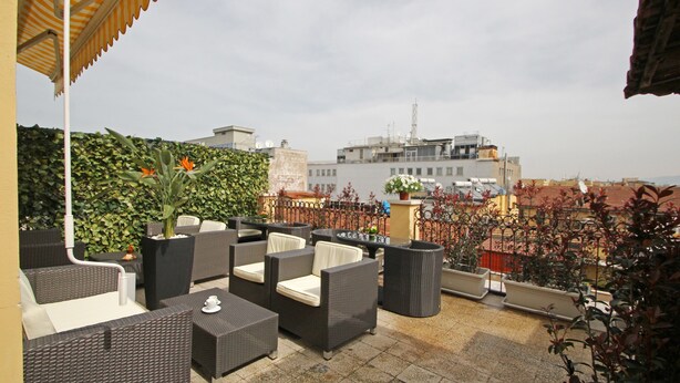 A rooftop terrace with wicker furniture, potted plants, and a view of buildings in the background. - Hotel Indipendenza (Rome)