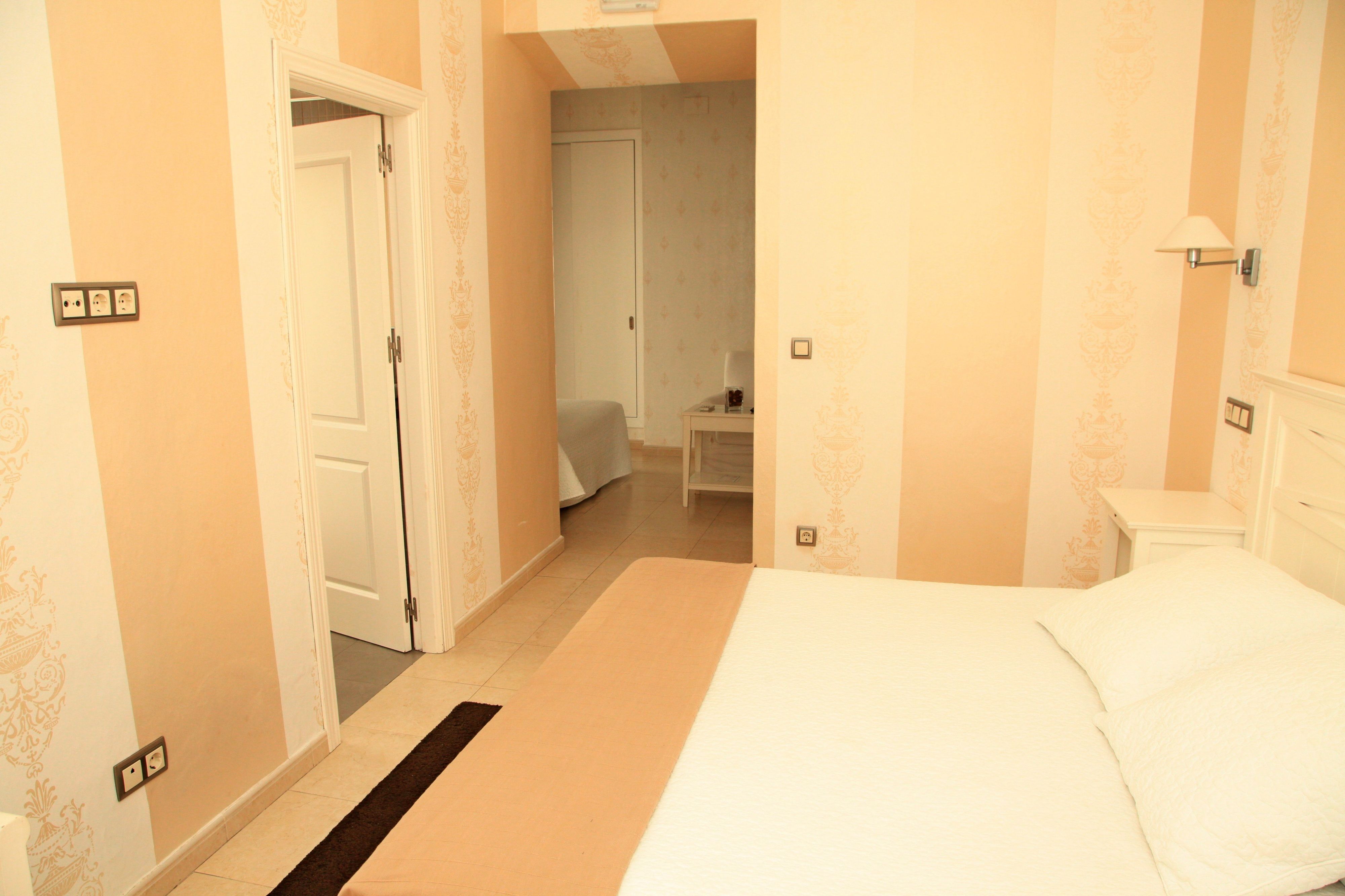 A hotel room with a bed, a bedside table, a nightstand, and a door leading to another room.