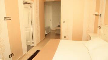 Quarto de hotel com cama, mesa de cabeceira e porta para outro cômodo.