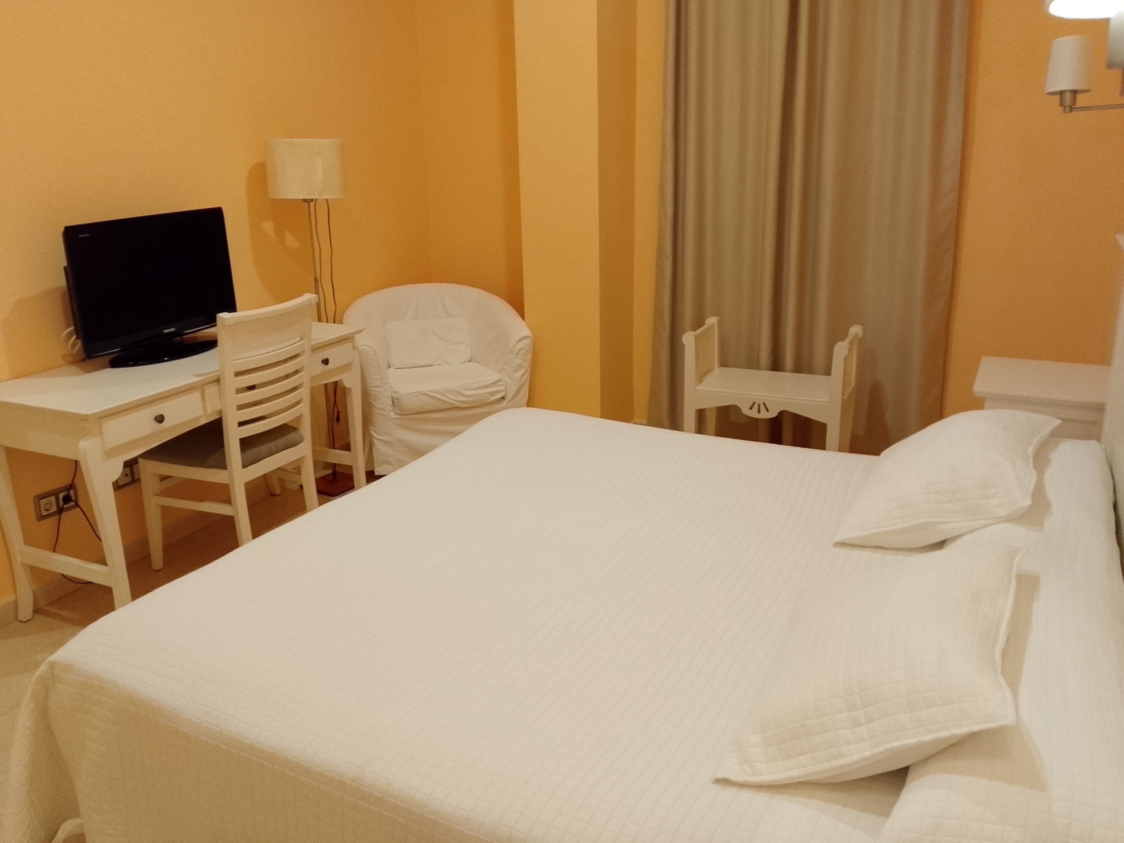 Een hotelkamer met een bed, een bureau met een computer, een stoel en een televisie.