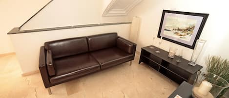 A modern living room with a brown leather sofa, a black console table with decorative items, and a framed picture on the wall.
