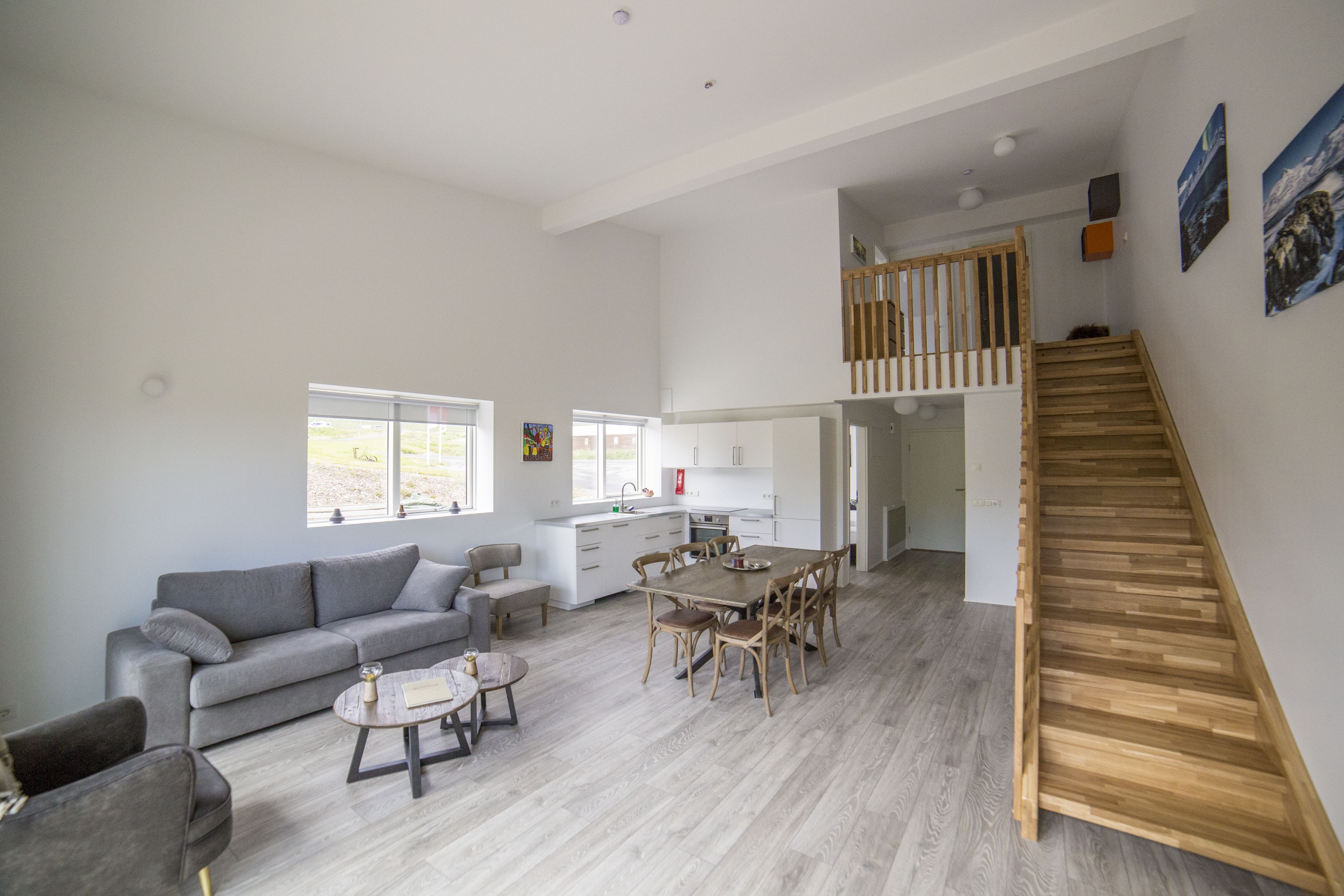 A spacious living area with a grey sofa, a dining table with chairs, and a wooden staircase.