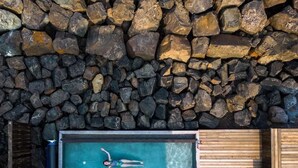 Un mur de pierre surplombe une piscine rectangulaire dans laquelle une personne nage.