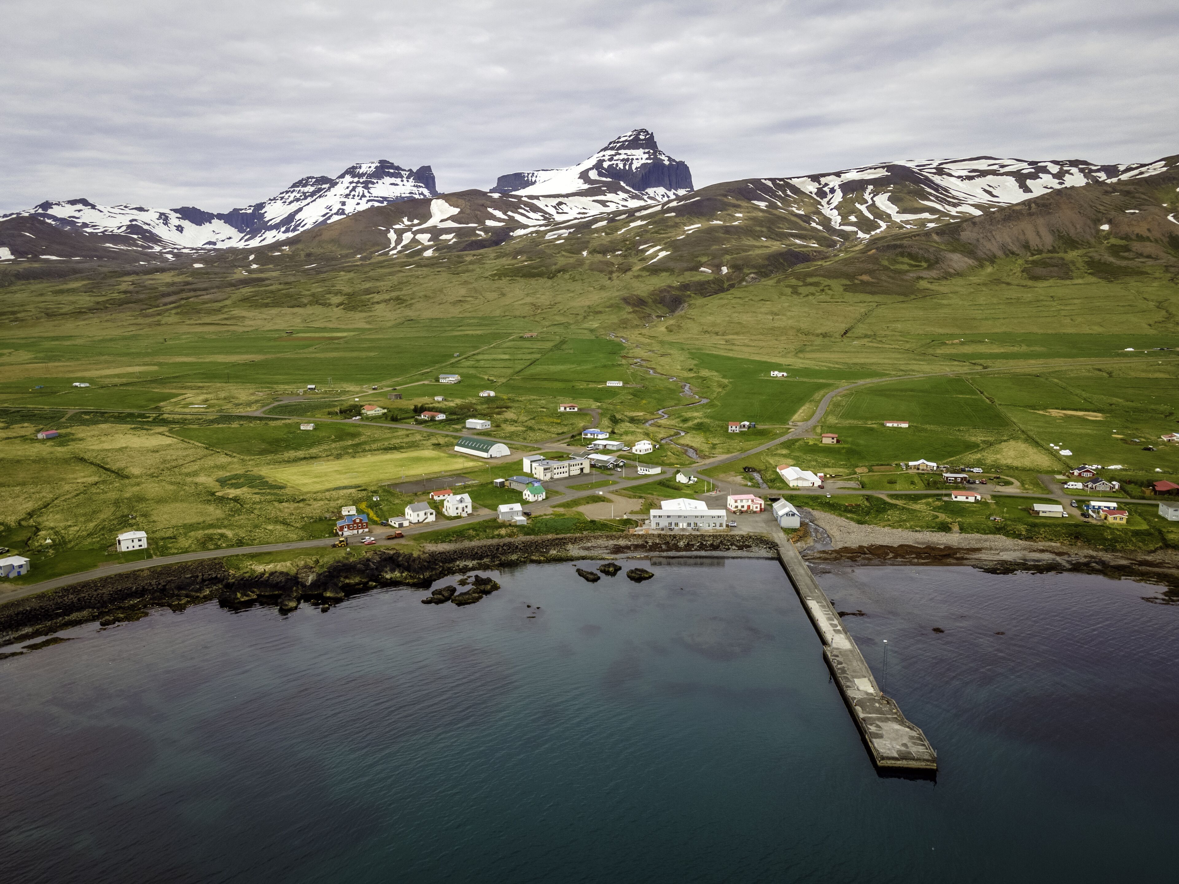 An aerial view of a coastal village with houses, a dock, and mountains in the background.