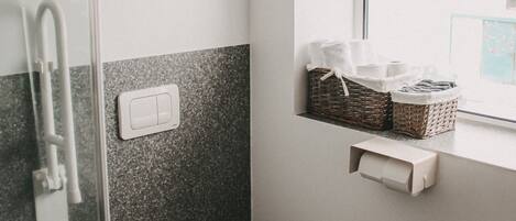 A bathroom with a shower, toilet, and a window with baskets on the sill.