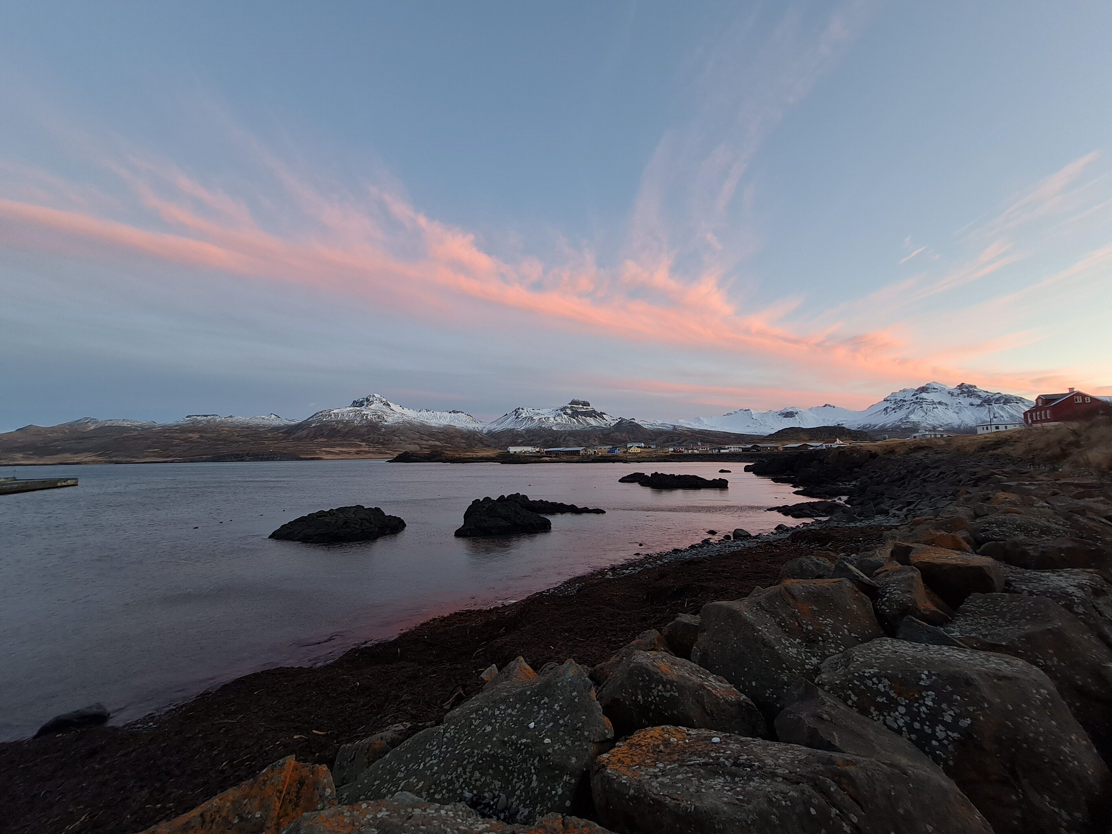 A coastal landscape with snow-capped mountains, rocky shoreline, and a clear sky.