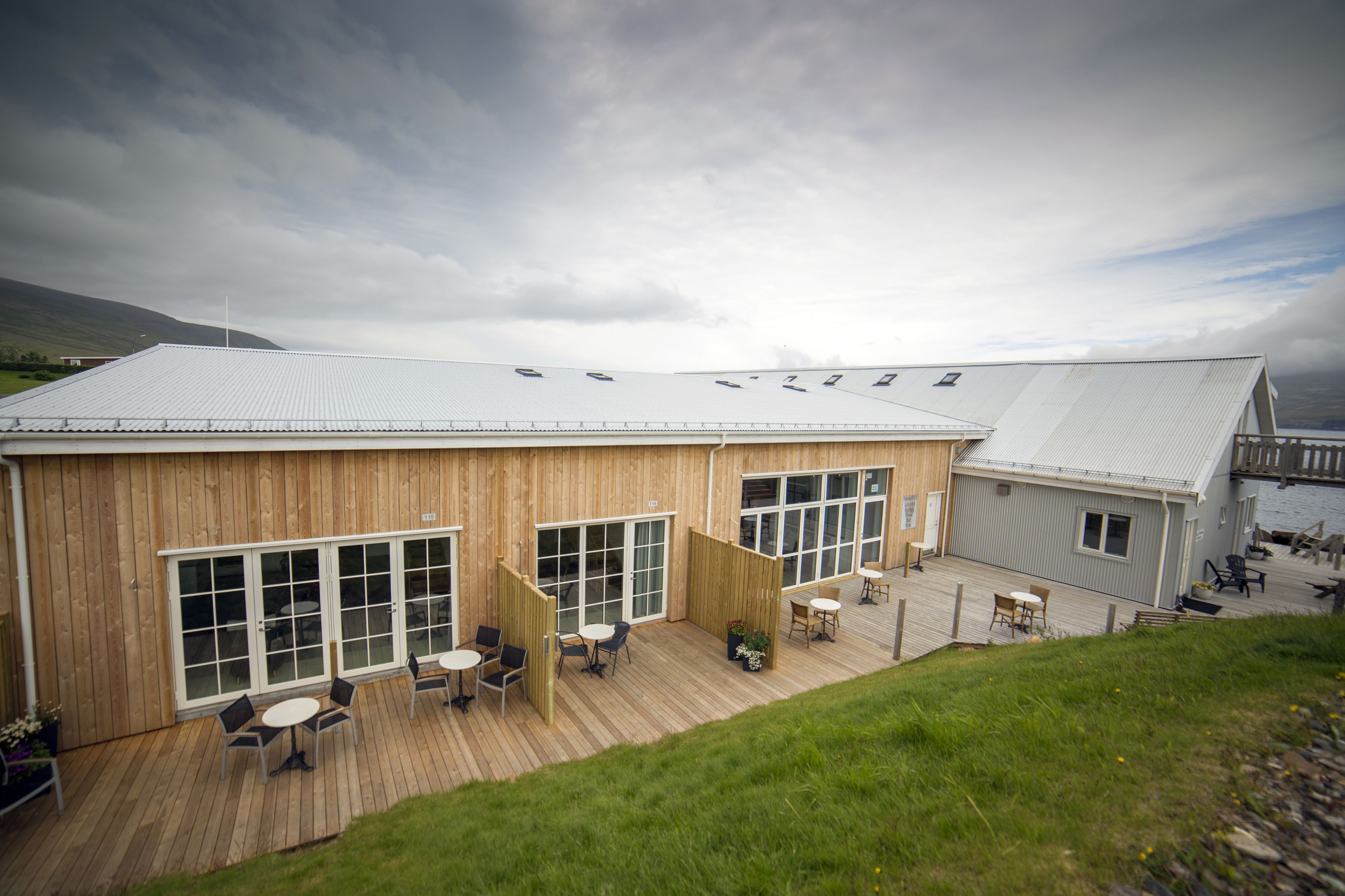 A wooden building with large windows and a deck area with outdoor seating.