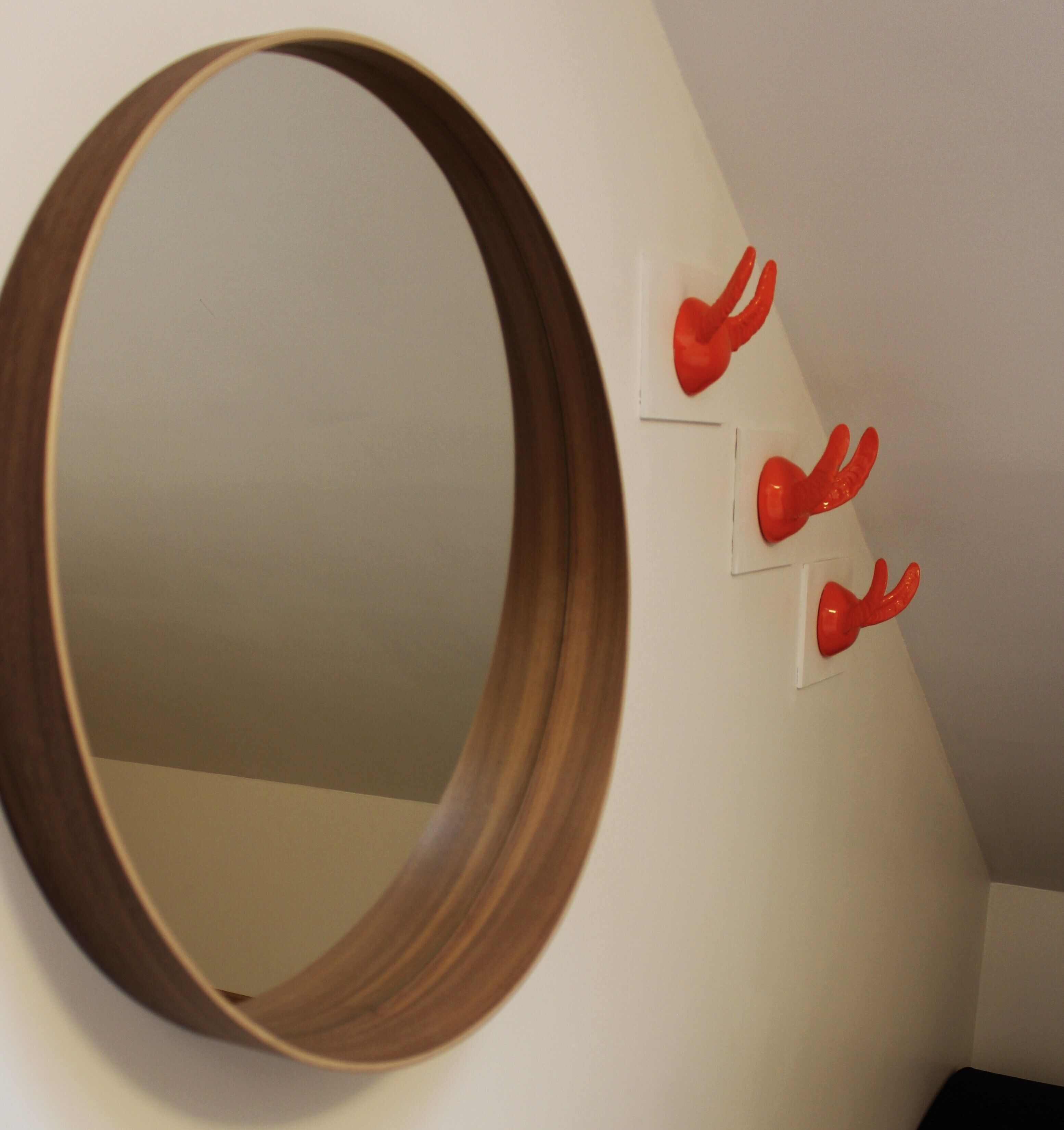 Una habitación con un espejo grande de marco de madera en la pared y tres objetos rojos colgados en la pared.
