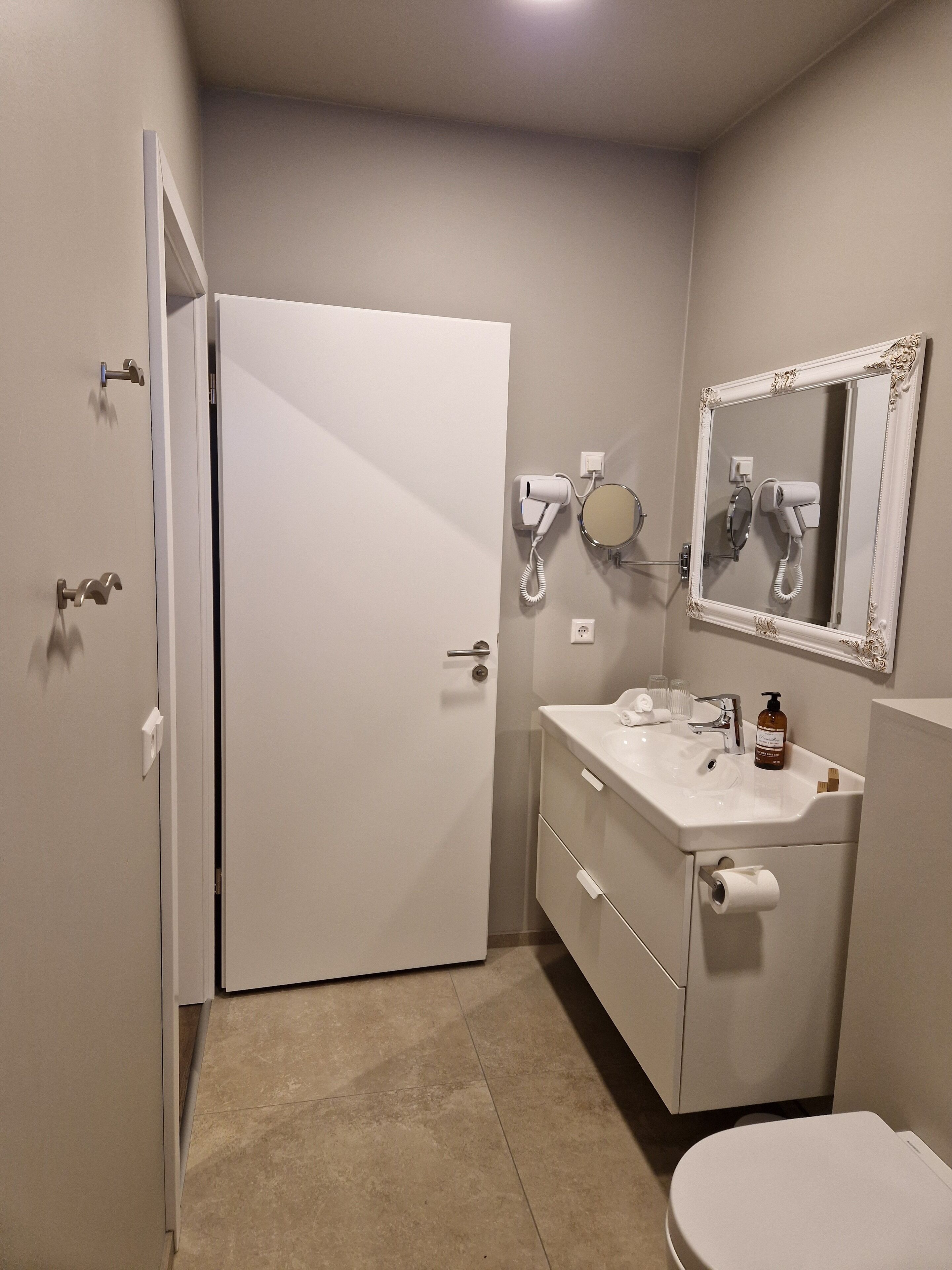 A small, clean bathroom with a white toilet, a sink with a mirror above it, and a hairdryer mounted on the wall.